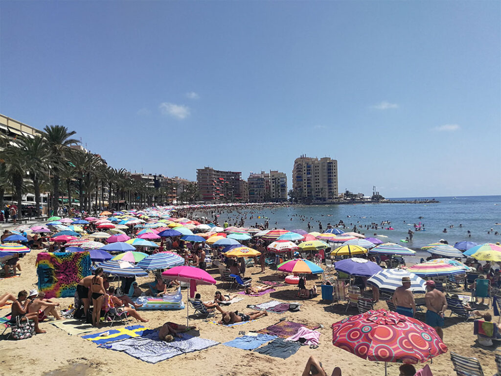 Människor som solar på stranden och under parasoller.